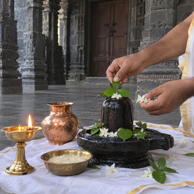 Bilva leaves and white flowers offered on a black stone Shivling with a ghee lamp