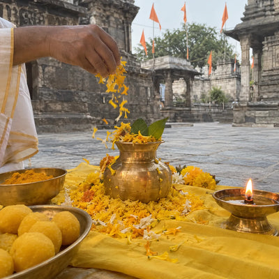 Yellow marigold petals, turmeric rice and a brass kalash on a yellow cloth for Baglamukhi pujan