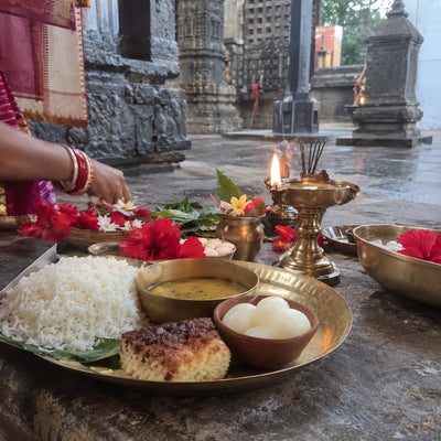 Odia bhog with chhena poda and rasagola, red hibiscus and a lamp