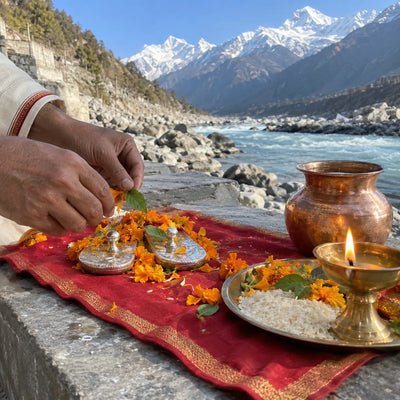 Marigold petals and a diya offered at small silver padukas, Himalayan river behind