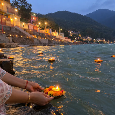 Hands releasing a leaf boat with a diya onto the Ganga at the evening aarti