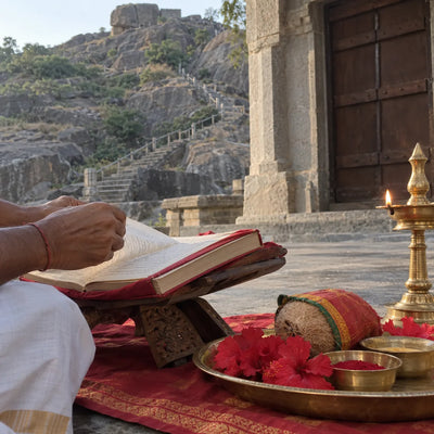 Scripture on a wooden stand with red hibiscus, a wrapped coconut and a samai lamp for Saptashati path