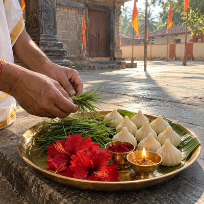 Durva grass bundles and rows of modaks on a banana leaf with red hibiscus and a diya