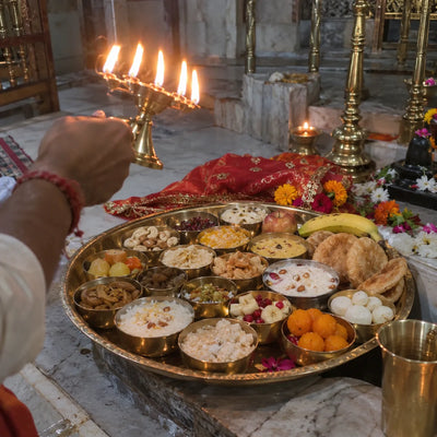 An aarti lamp raised over a thali of sixteen bhog bowls