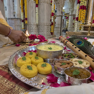 Saffron sweets and dry fruits with tulsi leaves, a flute and a peacock feather