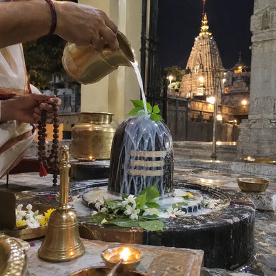Milk abhishek on a Shivling marked with bhasma, a rudraksha mala in hand