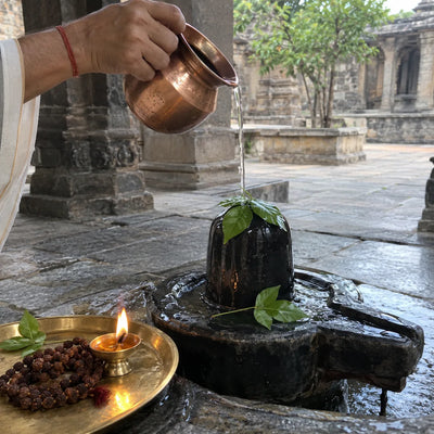 Water poured over a Shivling with bilva leaves, with a rudraksha mala and a ghee diya beside it