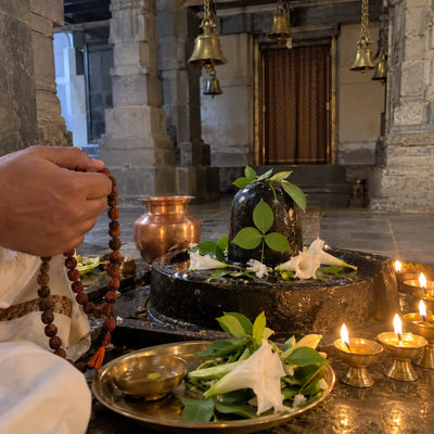 Rudraksha mala beside a Shivling with bilva leaves and brass lamps for Maha Mrityunjaya jaap