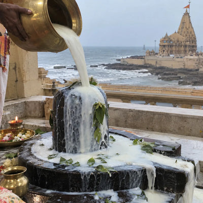 A steady stream of milk poured over a Shivling, sea and temple behind