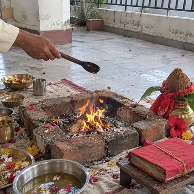 Ghee offered into a havan fire with red hibiscus and a chunri-wrapped coconut