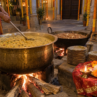 Large vessels of khichdi and halwa cooking for a temple bhandara, with stacks of leaf plates