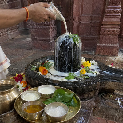 Panchamrit abhishek with five offering bowls before carved red-stone walls