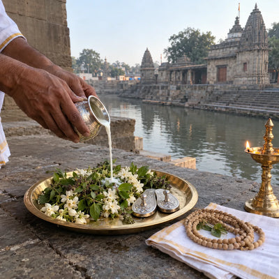 Milk poured over tulsi and white flowers beside silver padukas and a samai lamp