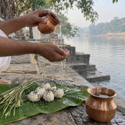 Pindas with sesame and kusha grass on a banana leaf as water is offered through the fingers