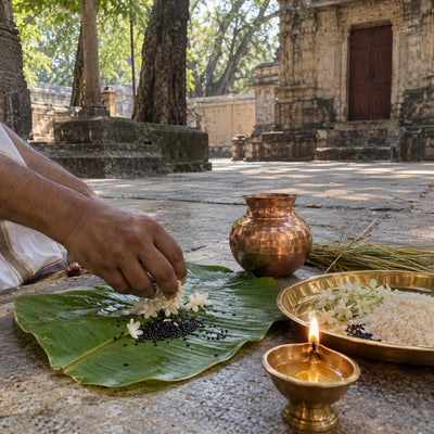 White flowers and black sesame on a banana leaf with a copper kalash, kusha grass and a diya