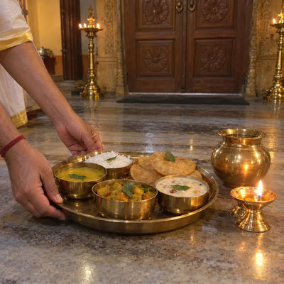 A brass rajbhog thali of dal, rice, sabzi, kheer and puris, each topped with a tulsi leaf