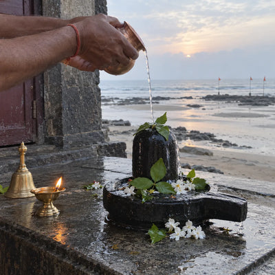 Water poured over a black stone Shivling with bilva leaves by the sea at low tide