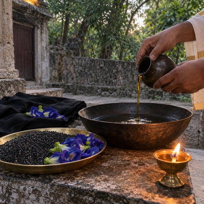 Sesame oil poured into an iron bowl with black sesame, blue flowers and an oil diya for Shani puja