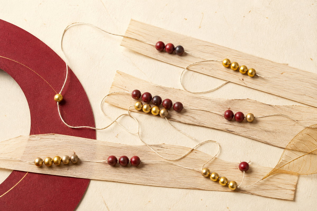 Conceptual illustration of small maroon and gold bead groups arranged on palm-leaf paper strips and linked by cotton thread, evoking meditative counting.