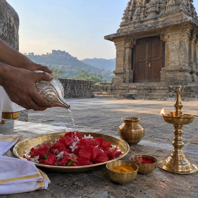 Water poured from a silver conch onto red flowers in a brass plate for abhishek puja