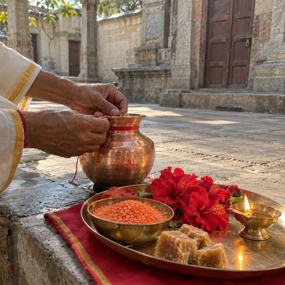 Red thread tied on a copper kalash beside red lentils, red flowers and jaggery