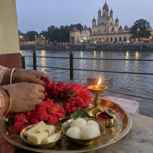 Red hibiscus garland and Bengali sweets offered with a brass lamp