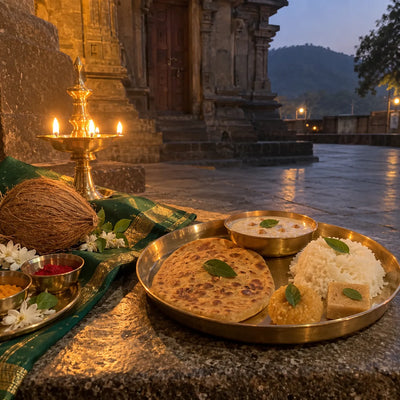 Brass thali of bhog with kheer and sweets beside a green sari piece, coconut and samai lamp