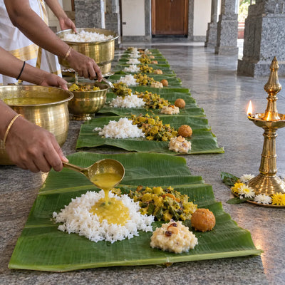A row of banana-leaf plates served with rice, dal and sweets from brass vessels
