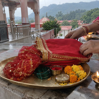 Red chola with a gold border, a chunri and bangles on a brass plate