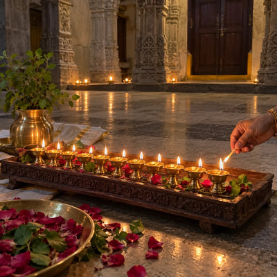 Eleven glowing brass ghee lamps on a wooden tray with tulsi leaves and rose petals