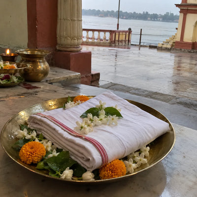 A folded white dhoti with flowers and tulsi on a brass plate