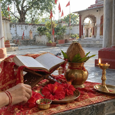 Open scripture on a wooden stand with a red chunri, hibiscus and a brass kalash for Chandi path