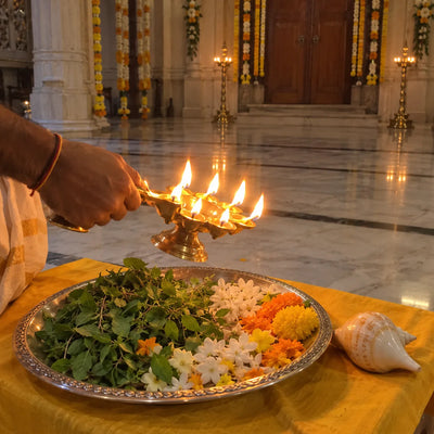 A five-wick ghee lamp circled over tulsi leaves and flowers for an Ekadashi aarti