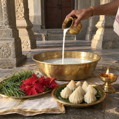 Milk poured from a brass lota into an abhishek bowl with durva, hibiscus and modaks