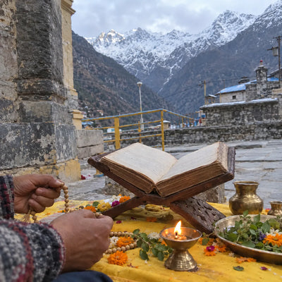 Open scripture on a wooden stand with a tulsi mala and a diya, Himalayan peaks behind