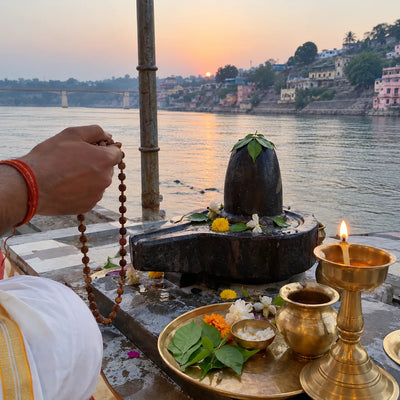 Rudraksha mala and ghee lamp beside a Shivling, the Narmada at dawn