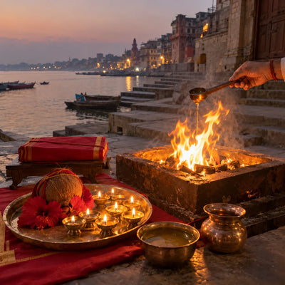 Ghee offered into a havan fire beside a scripture, red hibiscus and nine diyas