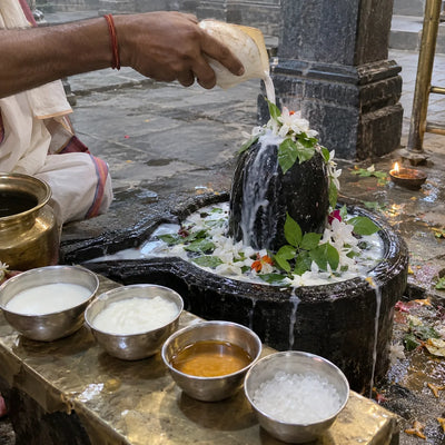 Panchamrit poured from a conch over a Shivling with bilva leaves