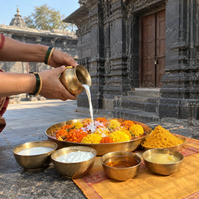 Hands pouring panchamrut over marigolds beside bowls of milk, curd, honey, ghee and turmeric