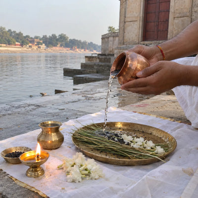 Water with black sesame offered over kusha grass beside a ghee lamp and white flowers