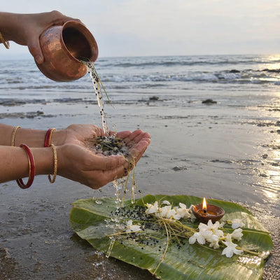 Water with sesame seeds poured from cupped hands for tarpan, with white flowers and a diya