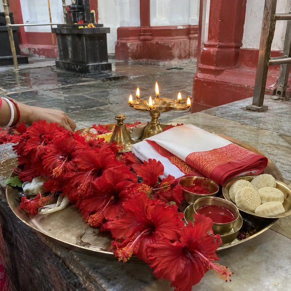Red hibiscus garland, red-bordered saree, sindoor and sweets for Kali puja