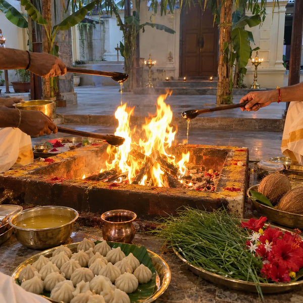 Several hands offering ghee into a large havan fire surrounded by modaks and flowers