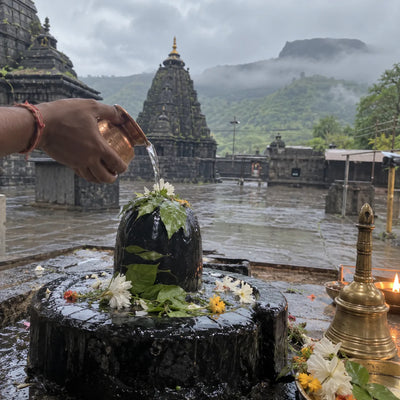 Rudrabhishek on a Shivling, black stone temple and misty hills behind