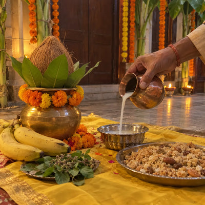 Panchamrit poured into a silver bowl beside a kalash, bananas, tulsi and panjiri on yellow cloth