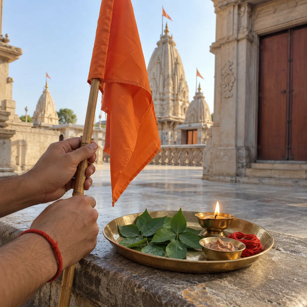 A saffron cloth flag on a bamboo staff beside bilva leaves, red thread and a lit diya