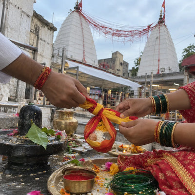 Hands tying a gathbandhan knot with sindoor, bangles and bilva leaves