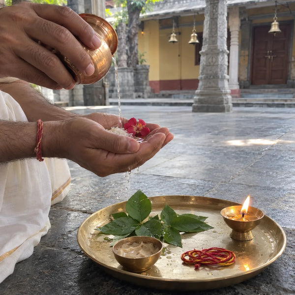 Water, rice and a flower held in a cupped palm for a sankalp above a brass puja plate