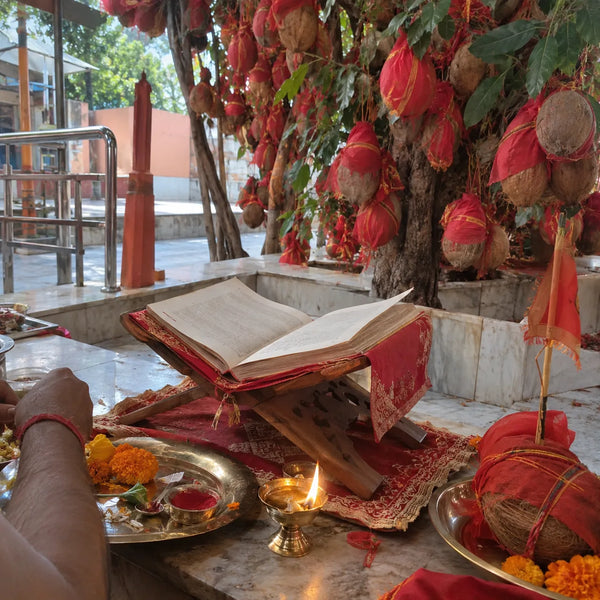 Scripture on a stand with a diya, sindoor and a red-wrapped coconut